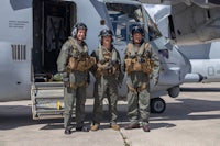 three military personnel standing in front of a plane