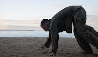 a man bending down on the sand